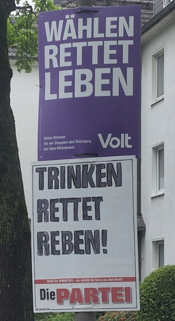 Ein lila Wahlplakat mit der Aufschrift „Wählen rettet Leben“. Darunter ein Plakat von Die PARTEI mit der Aufschrift „Trinken rettet Reben“. 